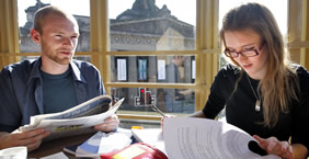Two students sitting in a cafe looking through notes and papers.