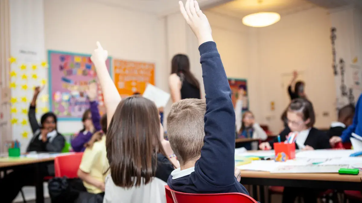 Two young students raise their hands in a classroom at IntoUniversity's centre inCraigmillar, Edinburgh