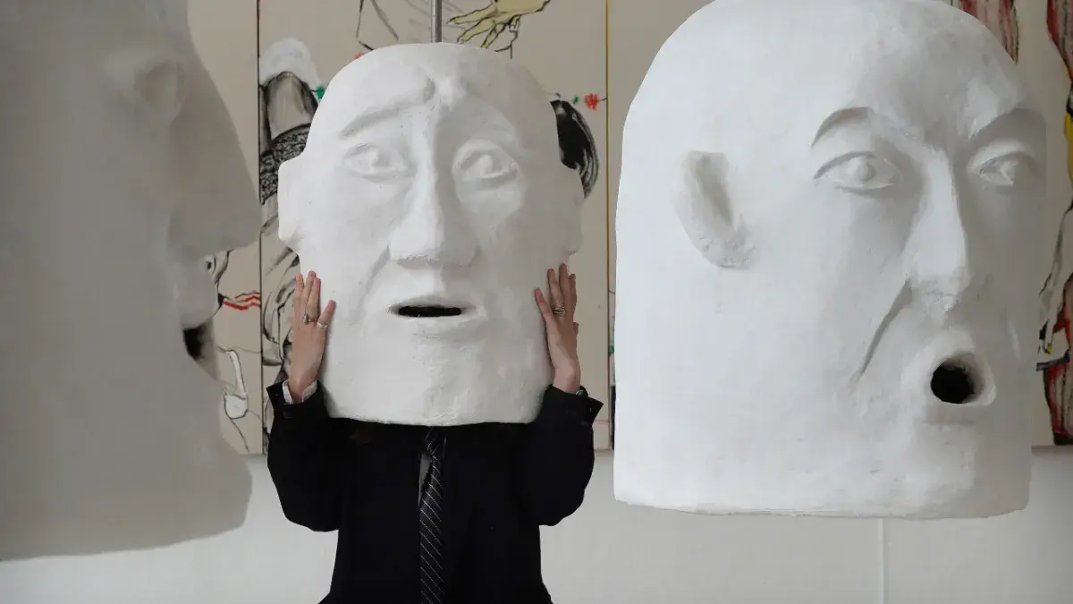 An ECA graduate wears a large white 'head' sculpture that they designed.
