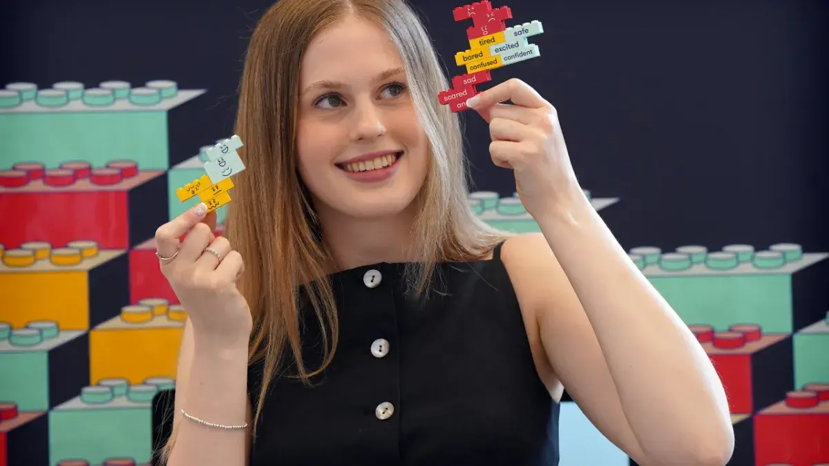 An ECA graduate poses with lego kits they created deigned to help people with Down's Syndrome learn about consent.