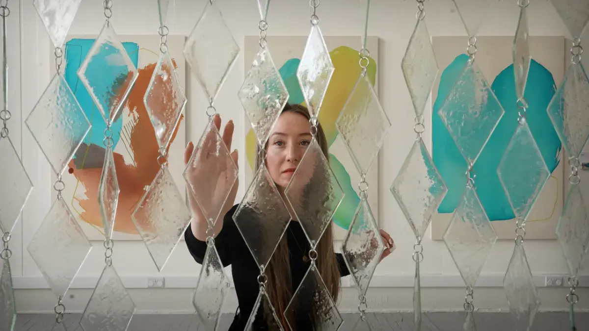 An ECA graduate approaches a sculpture that they designed made of glass and steel.