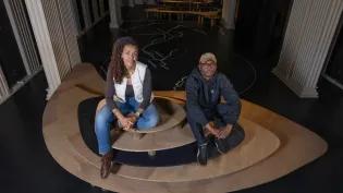Artist collective MADEYOULOOK pictured sitting on a wooden earthwork sculpture in their installation. 