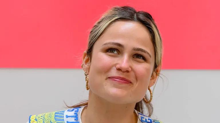 Graduating student Poppy Morgan wearing a blue and yellow collar in front of a pink backdrop with a white collar suspended in front of it