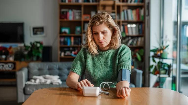 White middle-aged woman wearing short sleeved green jumper measuring her blood pressure at home
