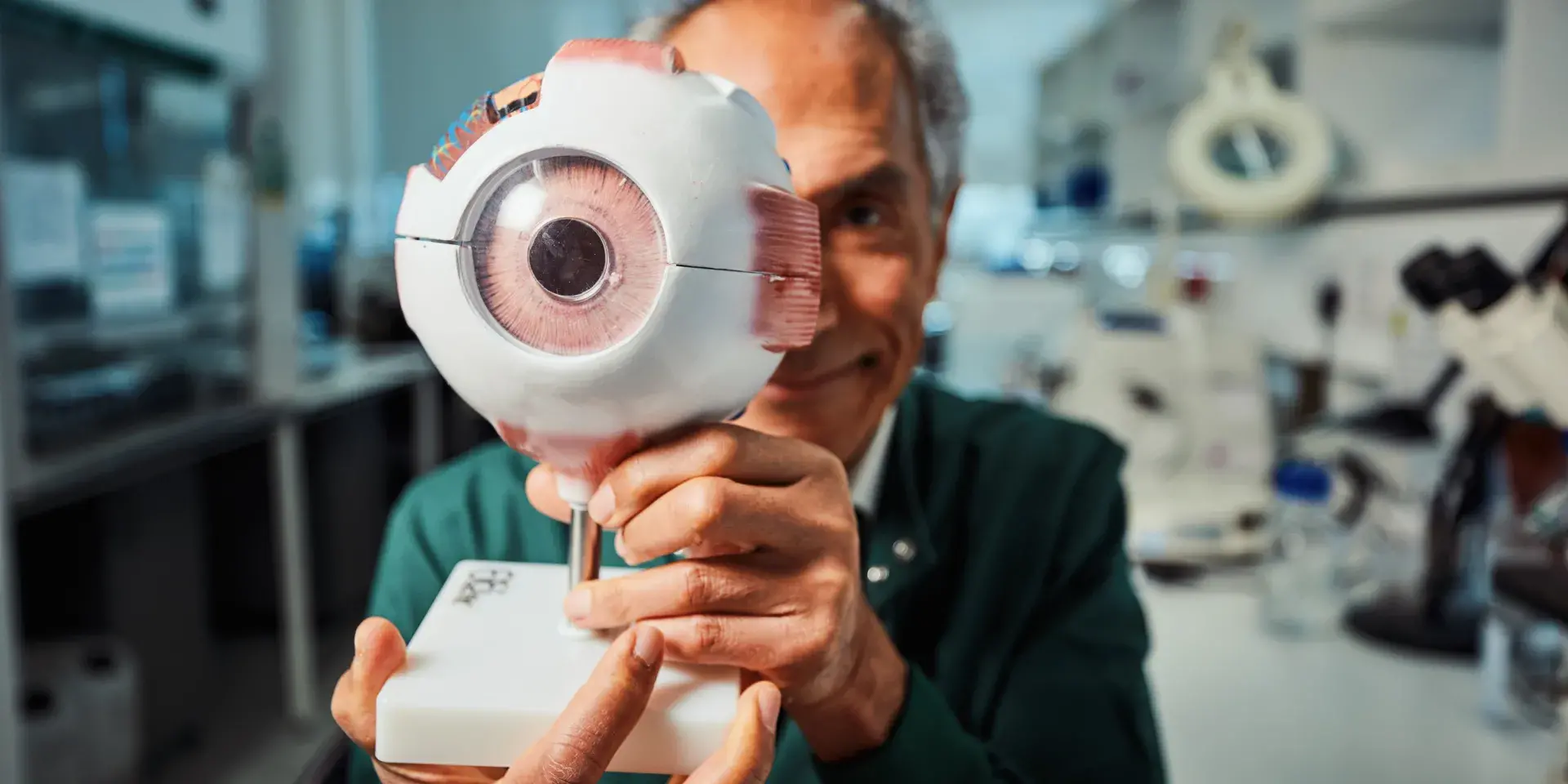 A researcher from the University of Edinburgh sitting in a lab holding a model of an eye