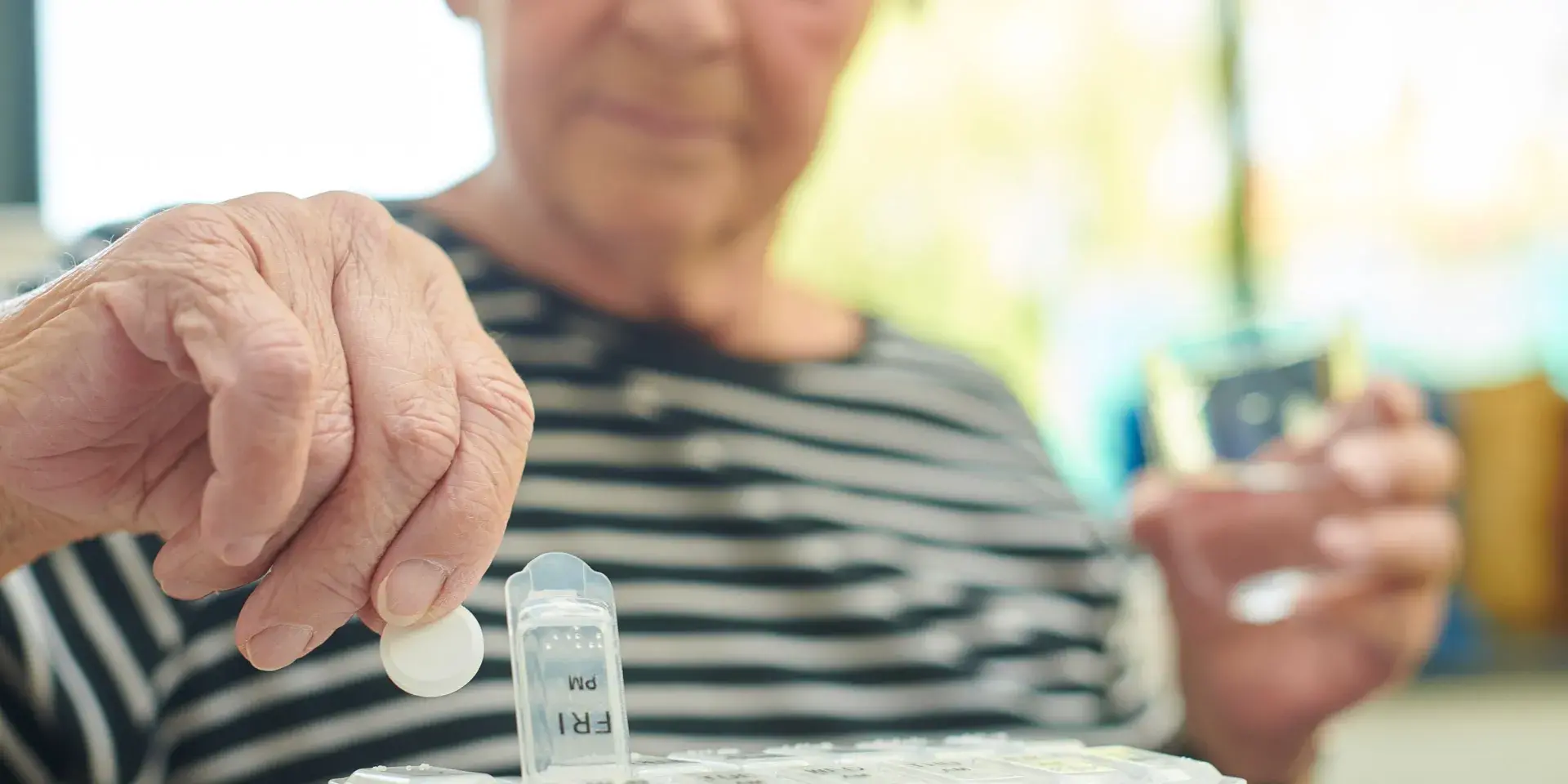 Senior woman wearing striped t-shirt takes the days tablets with a glass of water