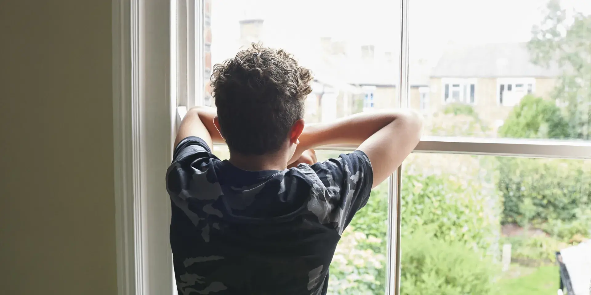 Teenage boy wearing dark t shirt looking out of bedroom window