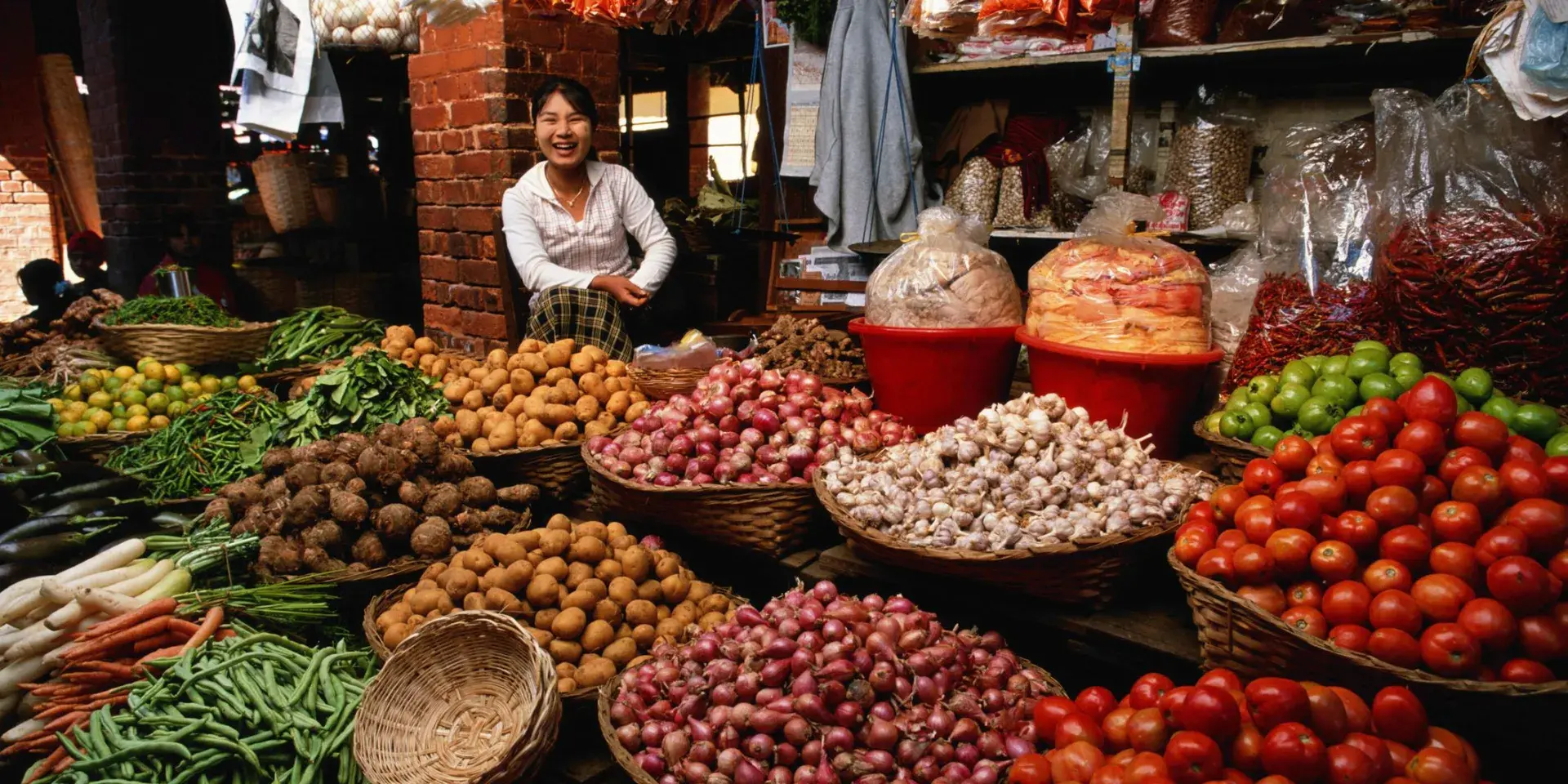 Woman smiling behind an abundance of colourful food at her market stall