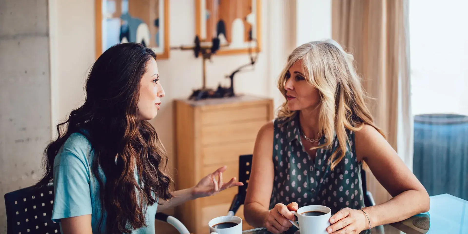Two women sitting at a table and talking while drinking coffee