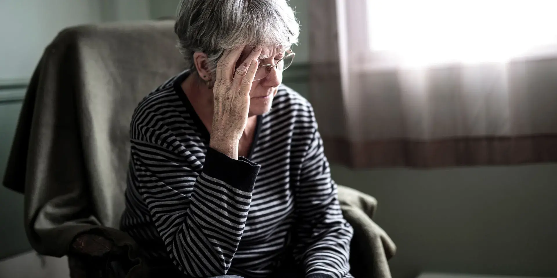 An elderly woman at home looking worried with her head in her hands