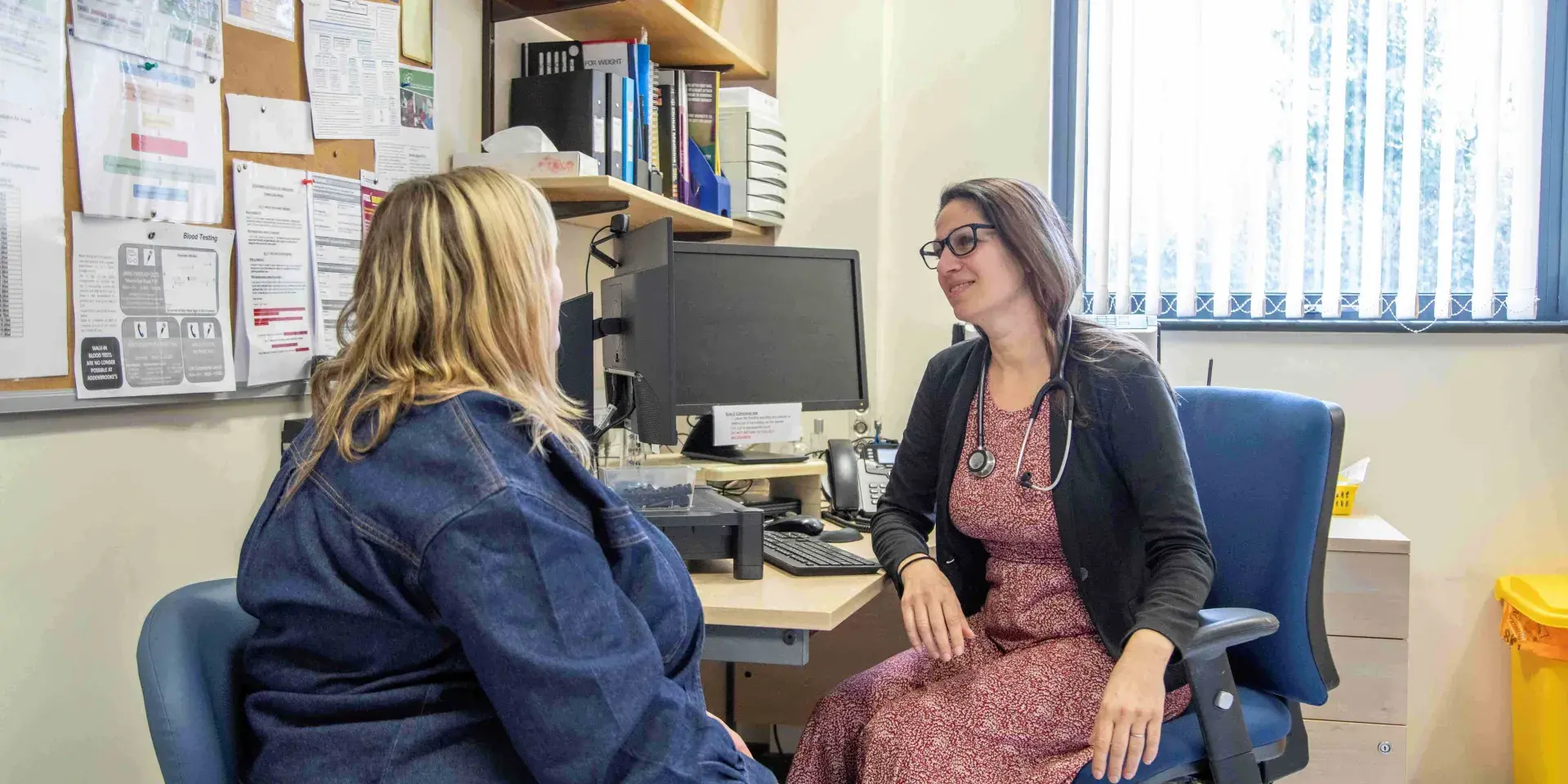 A woman is seen from behind talking to her female GP