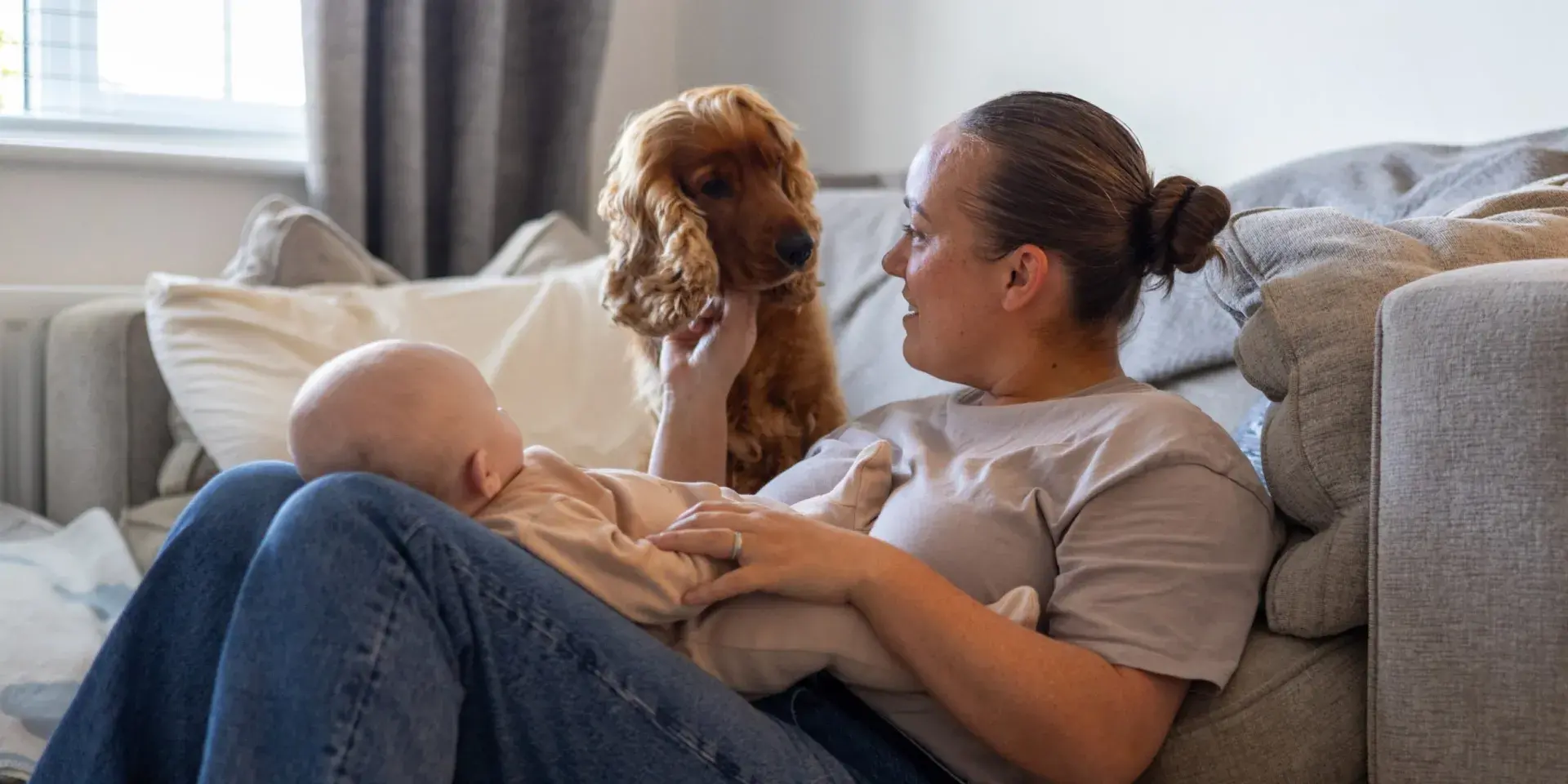 Mother sat in the floor holding newborn baby, with family dog watching nearby