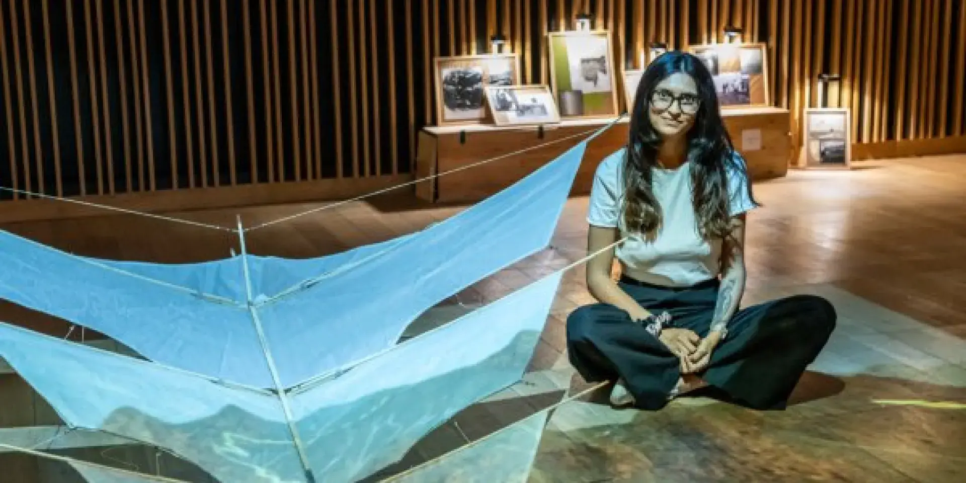 Artist sitting on floor next to exhibit of a kite