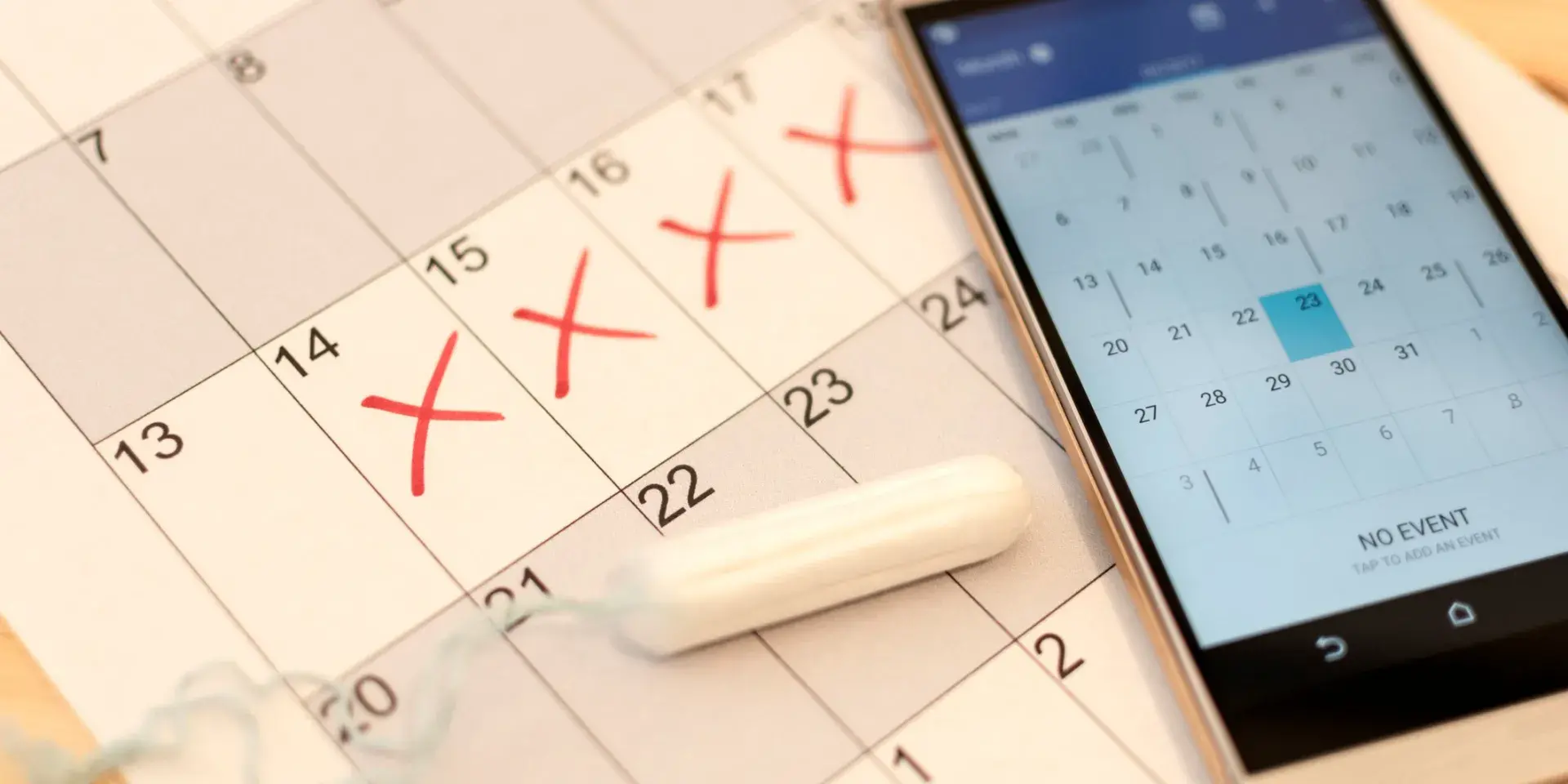 Image of a tampon and smartphone calendar on top of a paper calendar depicting menstrual cycle