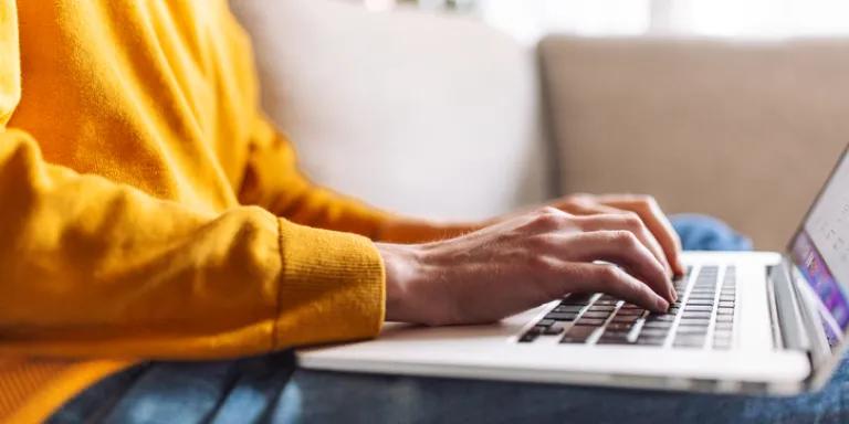 person in a yellow jumper typing on a keyboard