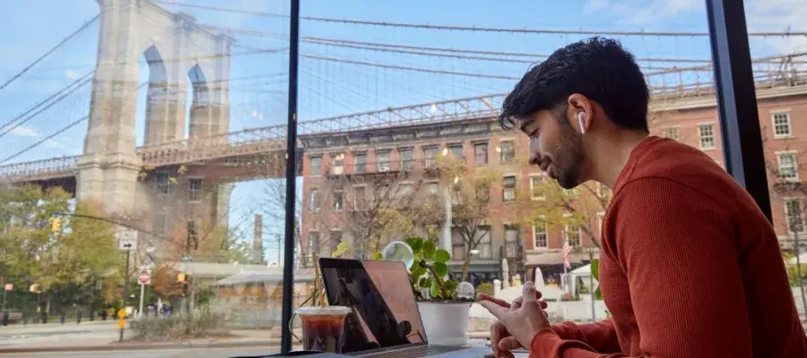 Someone on a laptop in a cafe. Out the window in the background is the Brooklyn Bridge.