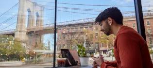 Someone on a laptop in a cafe. Out the window in the background is the Brooklyn Bridge.