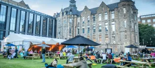 People sit at benches and seating outside at the Edinburgh International Book Festival, held at Edinburgh Futures Institute in 2024