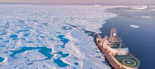 Aerial view of research ship next to very large section of sea ice