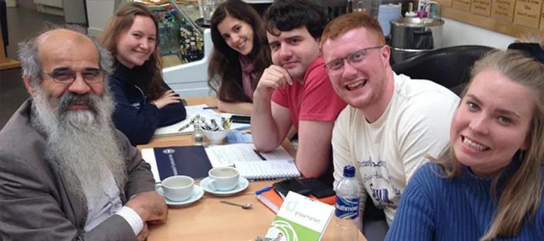 6 people sit around a table and smile to camera