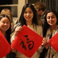 Three students hold up Chinese characters on painted in black on red squares of paper