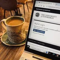 A coffee on a wooden table beside a laptop showing the MyEd homepage