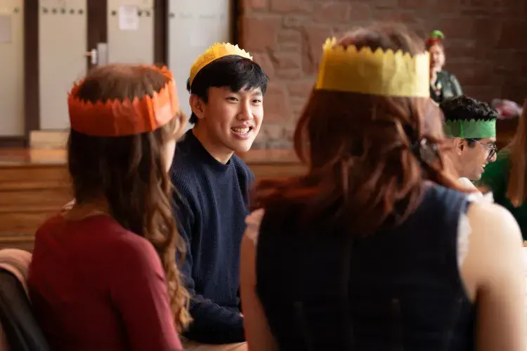 Students sit around a table wearing festive hats