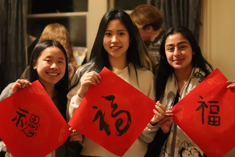 Three students hold up Chinese characters on painted in black on red squares of paper
