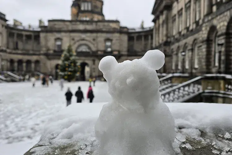 A miniature snowman in the shape of a bear sits on a stone handrail in Old College Quad
