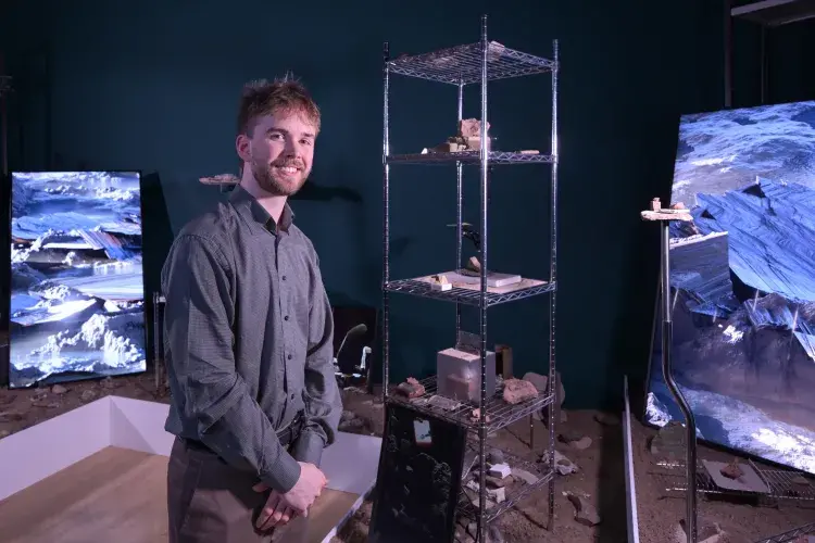 A student artist poses in front of their installation. 