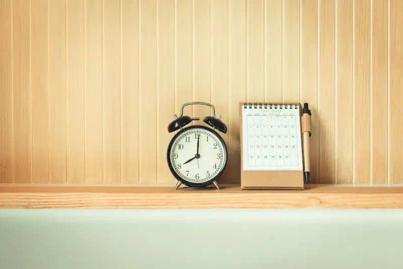 Image of an analogue alarm clock and calendar on a shelf