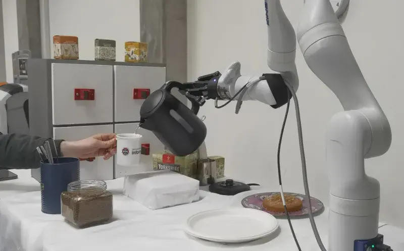 Coffee-making robot pours water from a kettle into a cup held by a person