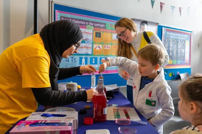 A festival volunteer helps a young boy perform a simple scientific experiment at the Edinburgh Science Festival