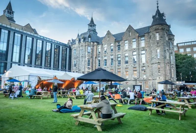 People sit at benches and seating outside at the Edinburgh International Book Festival, held at Edinburgh Futures Institute in 2024